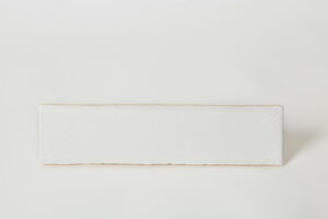 Biała płytka dekoracyjna typu cegiełka, z błyszczącą powierzchnią i abstrakcyjnymi wzorami.