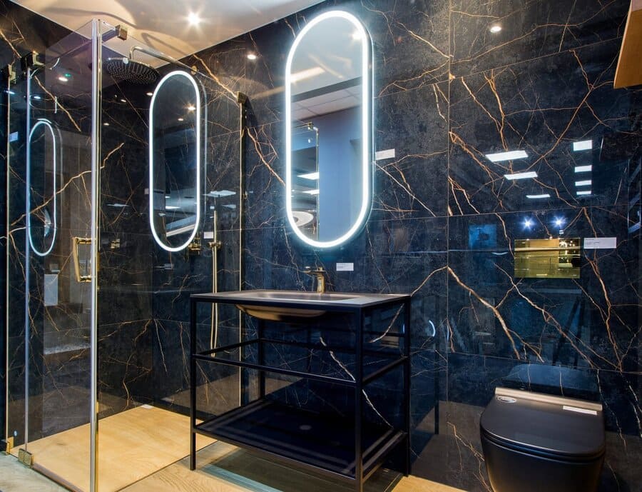 Łazienka z płytkami imitującymi czarny marmur - FLAVIKER Supreme Evo noir laurent lux 60x120. Błyszczące czarne płytki ze złotymi żyłkami na ścianie. Łazienka z lustrem, umywalką, prysznicem i ubikacją.