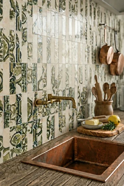 Zielone płytki majolika Marca Corona Miniature Fregio Verde Maiolica 6x24 na ścianie w rustykalnej kuchni z miedzianym zlewem i mosiężną armaturą.