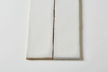 Kafel białe cegiełki, dekoracyjne z powierzchnią pokrytą geometrycznymi wzorami wystepującymi w 8 wariantach - Peronda Harmony Pasadena White 7,5x30cm. Na zdjęciu dwie białe płytki dekoracyjne w podłużnym kształcie.