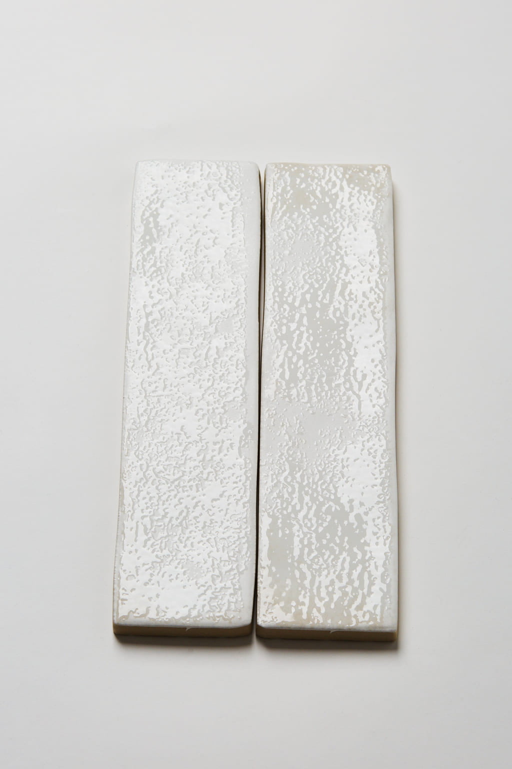 Hiszpańskie kafelki do łazienki białe cegiełki, Peronda Harmony SUNSET WHITE 6x25cm. Zdjęcie pokazuje błyszczącą strukturę powierzchni płytek ceramicznych, pokrytych niejednorodnie szkliwem.