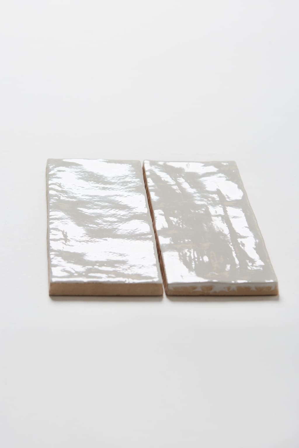 Dwie białe płytki ścienne, cegiełki z błyszczącą, nieregularną powierzchnią - Harmony RIAD WHITE 6.5x20cm. Płytki idealne do łazienki na ścianę lub jako fartuch kuchenny.