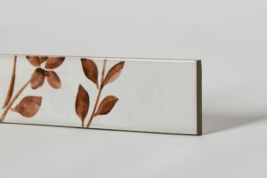 Glazura z motywem roślinnym - Peronda Harmony Aqua Brown decor 6x24,6cm. Płytki z białą powierzchnią i brązowym motywem kwiatowym.