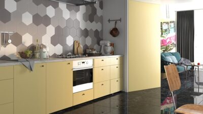 Kuchnia z płytkami heksagonalnymi na ścianie. Kafelki białe, szare i srebrne w matowym wykończeniu, nad żółtą szafką - fartuch kuchenny.