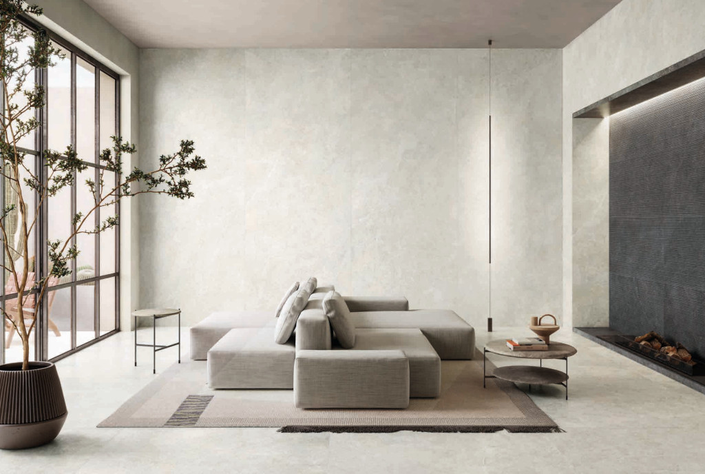 Płytki Impronta Limestone White na podłodze i ścianach jasnego salonu z narożną sofą i kominkiem obłożonym Limestone Dark Riga