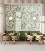 Kafelki motyw roślinny - Realonda OASIS 28.5x33 cm. Ściana w restauracji, pokryta płytkami heksagon z białym tłem i zielonymi liśćmi. Zielona sofa i dwa drewniane stoliki.