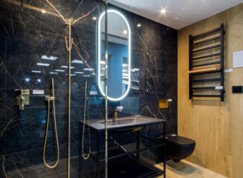 Płytki imitujące czarny marmur w łazience na ścianie FLAVIKER Supreme Evo noir laurent lux 60x120 cm. Włoskie płytki marmurowe, czarne ze złotą żyłką, elementy mosiężne armatury łazienkowej oraz drewniane płytki.