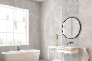 Płyty imitujące beton na ścianę 120x60 - Absolut Cozumel. Łazienka w szarych płytkach ceramicznych, biała wanna i umywalka, lustro, dekor ceramiczny za lustrem.