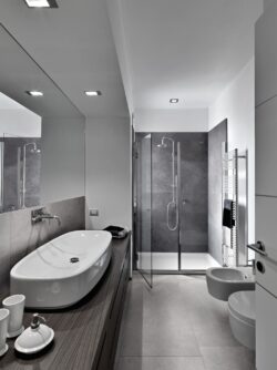 Szara łazienka z płytkami imitującymi kamień - SINTESI Ecoproject silver - podłoga, SINTESI Ecoproject smoke - ściana, prysznic.